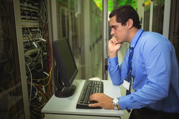 Technician working on personal computer while analyzing server in server room